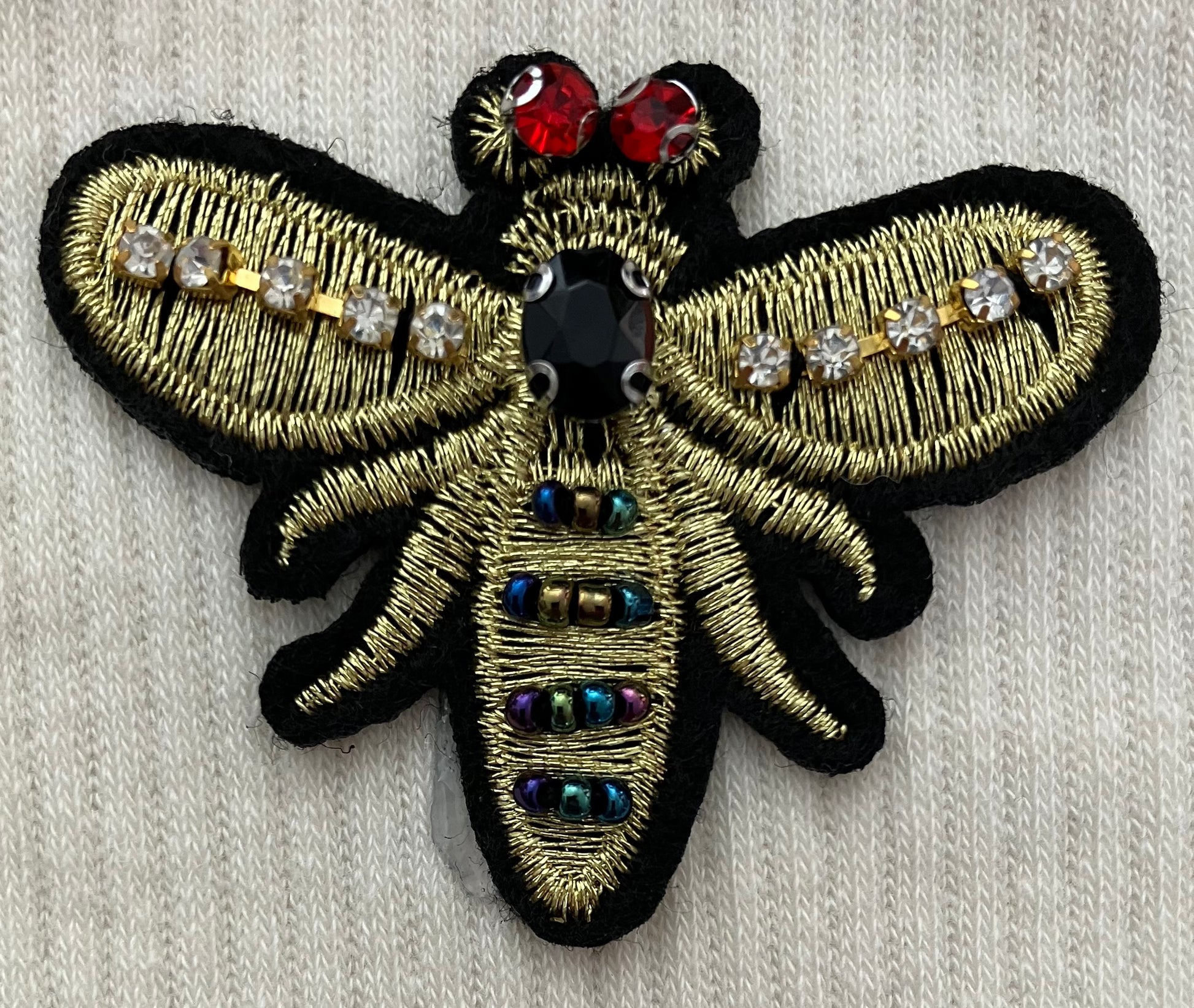 Embroidered bee patch with gemstones on a textured fabric background